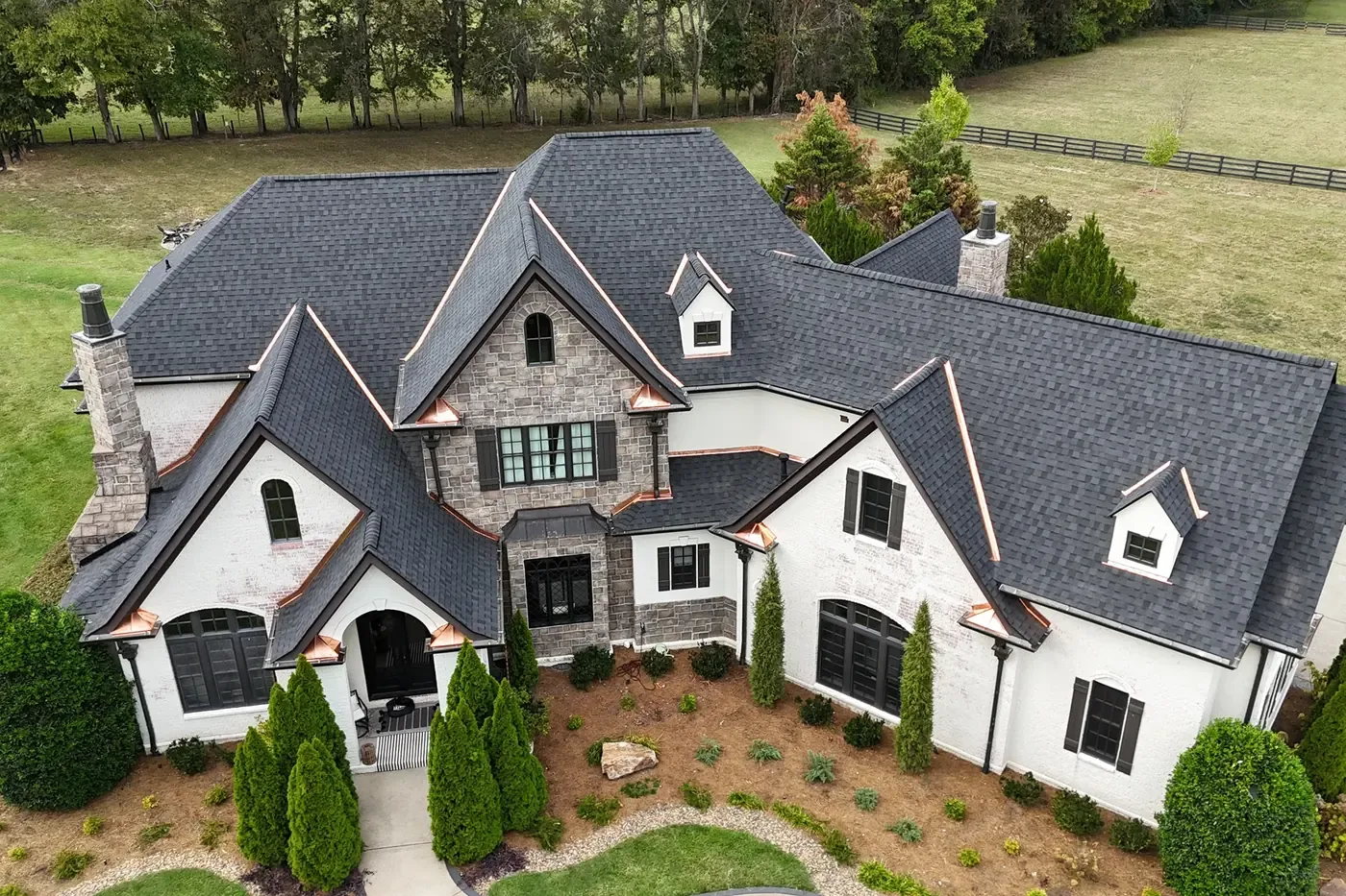 A drone view of a white brick house with a new black CertainTeed Landmark shingle roof, dormers and copper accents, above a fresh-cut lawn