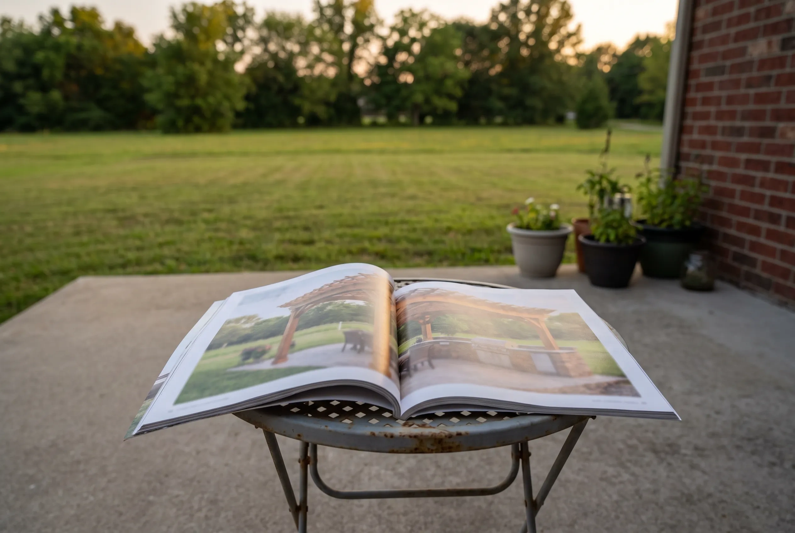 A magazine open to a photo of a cedar pergola, lying on a table on a bare concrete patio